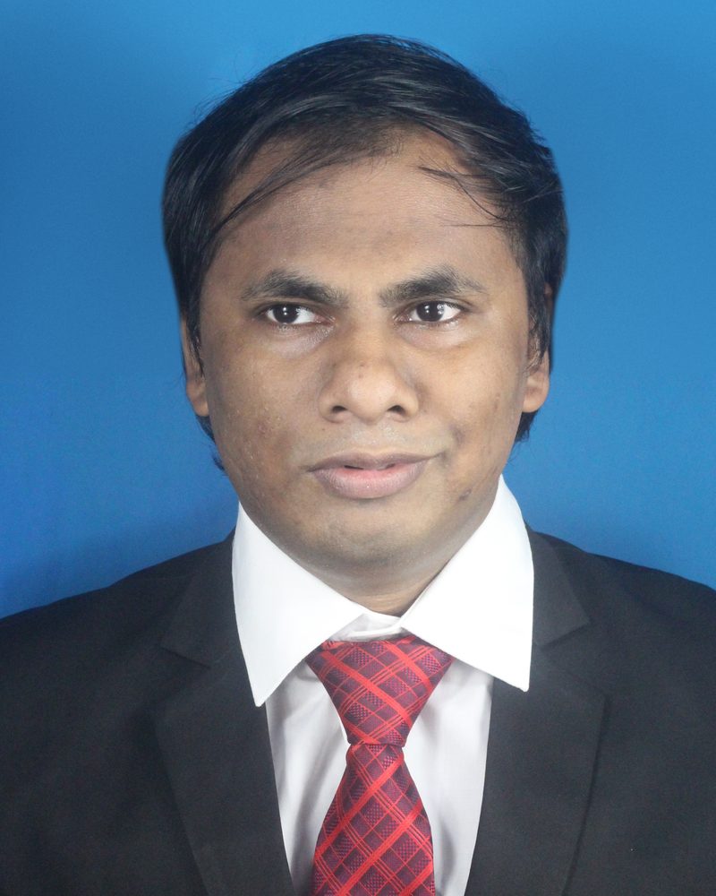 Portrait of Nazim Hossain in a dark suit, white shirt and red checked tie, against a blue background.